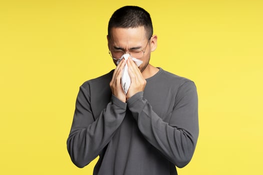 Sick young adult man blowing his nose with tissue paper photo