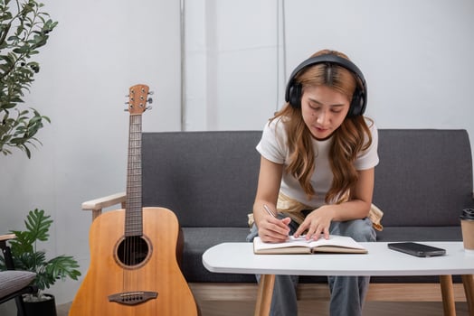 Young Female Artist Writing Songs with Guitar in Cozy Modern Living Room, Wearing Headphones for Inspiration photo