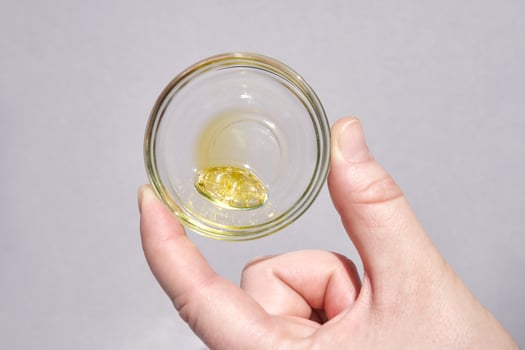 Hand holding clear glass cup with yellow liquid capsule on light gray background for supplement or health concept. photo