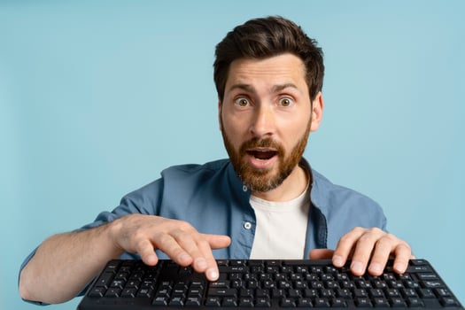 Shocked man looking at camera while typing on keyboard on blue background photo