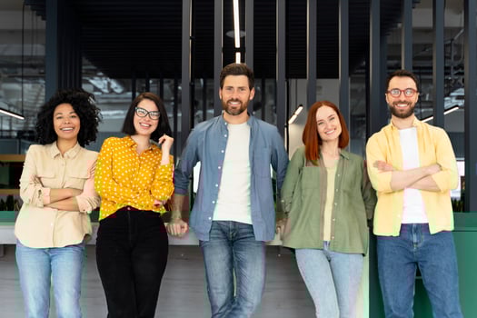 Five young professionals smiling while leaning on a counter in a modern office photo