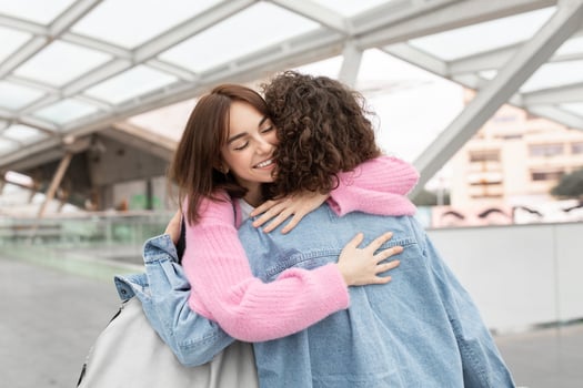 Two friends share a heartfelt embrace in a contemporary, well-lit environment, showcasing their joy and connection. The moment reflects a deep bond between them. photo