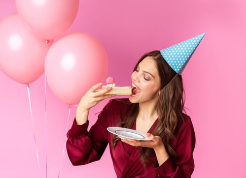 Birthday Lady Concept. Happy Young Woman In Party Hat Eating Piece Of B'Day Cake, Posing Over Colorful Background With Rosy Balloons photo