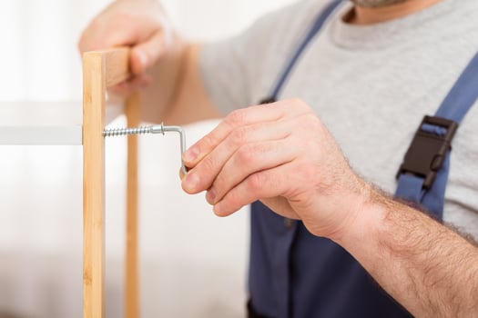 Furniture Assembling. Unrecognizable Carpenter Tightening Screws Fixing Cabinet Indoors, Wearing Blue Coverall. Cropped, Closeup photo