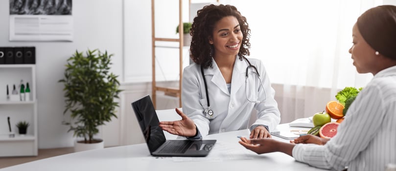 Smiling female african doctor nutritionist having conversation with her patient in front of laptop in clinic photo