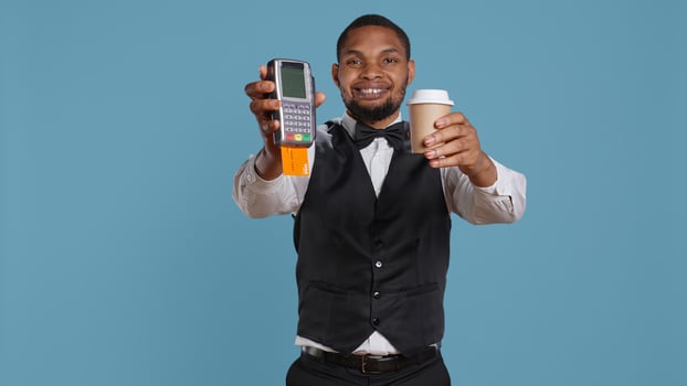 Hotel porter showing the pos terminal with card to symbolize electronic transaction at front desk. Bellboy with uniform receives payment for the lodging and amenities at the resort. Camera B. photo