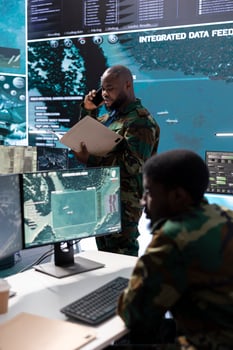 Army professional in command center talks on phone call and gives crucial information, overseeing satellite data in real time. Protect national security and support strategic military missions. photo
