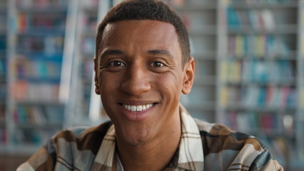 African American man student looking at camera toothy dental smile male ethnic library university study educational guy learning scholar college bookshelf academic bookworm reader intelligence smart photo
