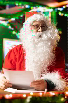 White bearded Santa Claus reviews letters from children by the fire, learning wishes for gifts and toys. North Pole mailbox overflows with holiday wishes, Christmas spirit shines bright. photo