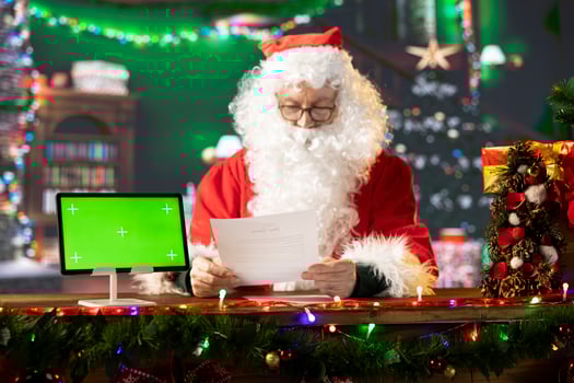 Santa Claus sitting next to copy space screen on device and reading letters from children around the world. Old man Saint Nicholas spreading his festive cheer for the holiday period. photo