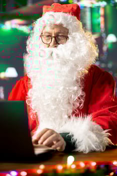 Father Christmas is navigating the web checking on children wish lists using his laptop. Festive North Pole cabin is filled with holiday cheer and online activity this x mas, checking the world map. photo