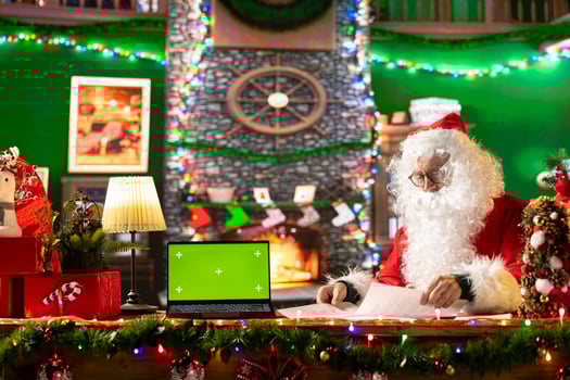 Santa Claus sitting next to copy space screen on device and reading letters from children around the world. Old man Saint Nicholas spreading his festive cheer for the holiday period. photo