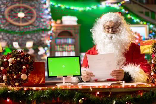 Father Christmas looking at his naughty or nice list next to isolated copy space screen, making preparations for x mas journey to bring gifts. Santa Claus reading wishes from children. photo