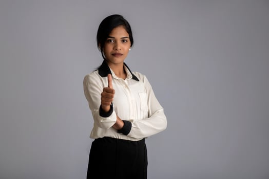 Young smiling girl showing ok sign or thumbs up on a grey background photo