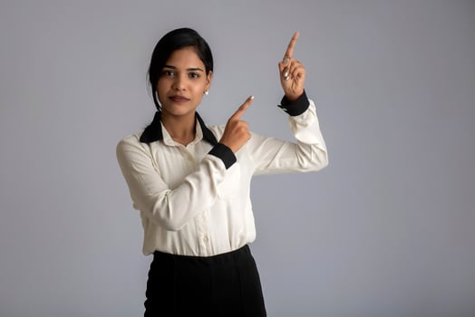 Young smiling girl pointing fingers to copy space on a grey background photo
