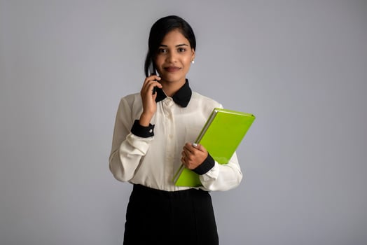 Pretty young girl holding book and using mobile on grey background photo