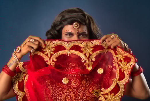 Young crossdresser man wearing Indian wedding clothes of a bride with bridal makeup and posing on grey background, looking fashion and glamorous. photo