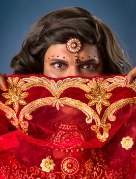 Young crossdresser man wearing Indian wedding clothes of a bride with bridal makeup and posing on grey background, looking fashion and glamorous. photo