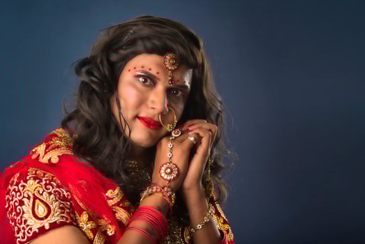 Young crossdresser man wearing Indian wedding clothes of a bride with bridal makeup and posing on grey background, looking fashion and glamorous. photo