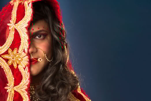 Young crossdresser man wearing Indian wedding clothes of a bride with bridal makeup and posing on grey background, looking fashion and glamorous. photo
