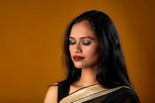 Portrait of a young beautiful girl wearing traditional black saree posing on a brown background. photo