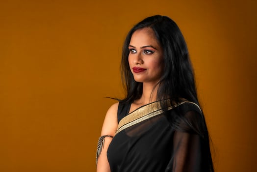 Portrait of a young beautiful girl wearing traditional black saree posing on a brown background. photo