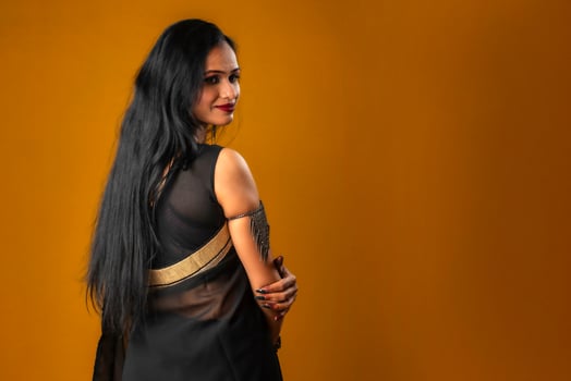 Portrait of a young beautiful girl wearing traditional black saree posing on a brown background. photo