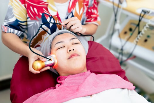 A woman is getting a facial treatment with a device that is emitting a light photo