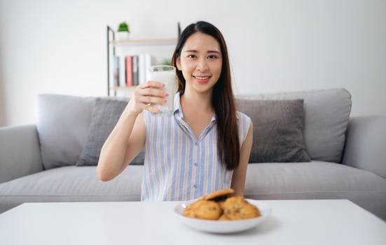 A woman is sitting on a couch with a glass of milk and a plate of cookies photo
