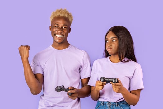 Happy African American guy and his upset girlfriend with game controllers on violet background photo