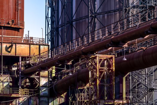 Rusty industrial pipes crisscrossing in front of storage tanks photo