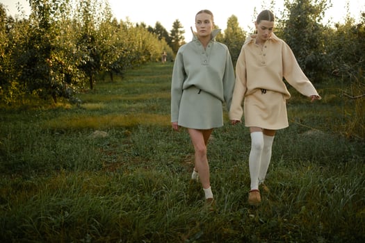 Two models in stylish tracksuits pose in apple orchard at sunset . The model is wearing a light-colored tracksuit and skirt photo