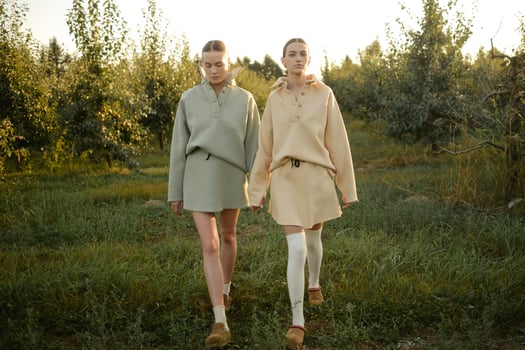 Two models in stylish tracksuits pose in apple orchard at sunset . The model is wearing a light-colored tracksuit and skirt photo