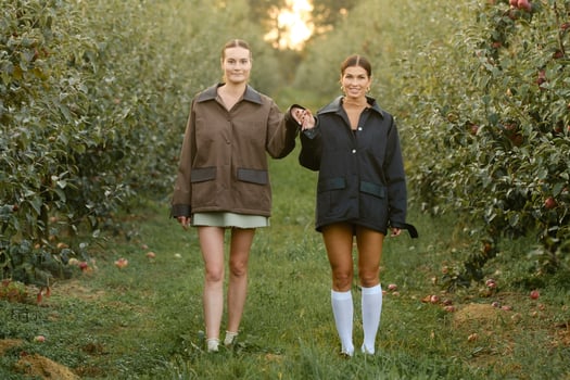 Two stylish girls in jackets at a fashion show in the apple orchard. Fashion show in the garden photo