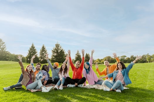 Group of diverse young adults waving and smiling outdoors in the park photo