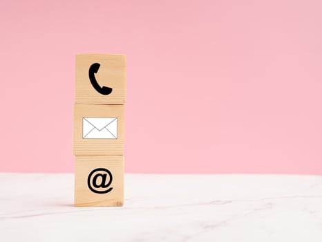 Wooden cubes with symbol telephone, email, address on a marble floor against a light pink background photo