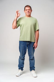 A man with a slight smile making an OK hand gesture against a neutral background photo