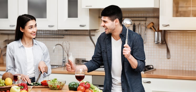 Defend Yourself. Playful guy pretending to fight with his wife using utensils, woman cooking healthy vegetable salad photo