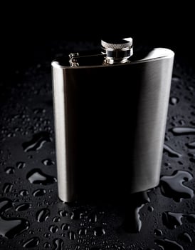 Flat stainless steel flask on a black background with water drops. photo