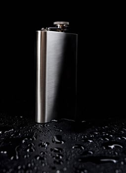 Flat stainless steel flask on a black background with water drops. photo