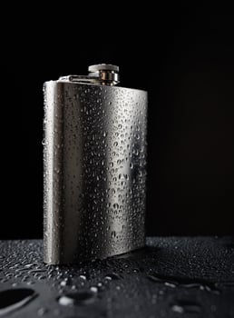 Stainless steel flask on a black background with water drops.Personal flat flask. photo