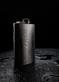 Stainless steel flask on a black background with water drops.Personal flat flask. photo