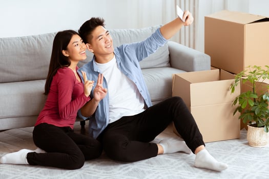 New Home, Technology Concept. Happy asian couple taking selfie with smartphone sitting on floor among cardboard boxes photo
