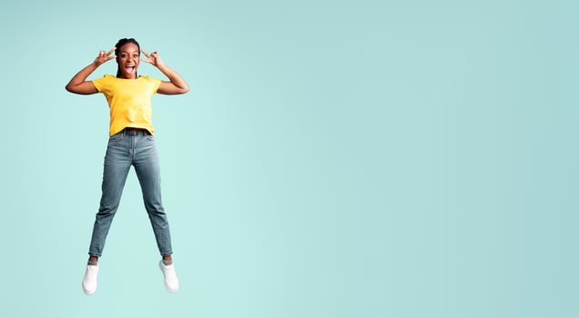 Joy Of Victory. Cheerful African American Lady Jumping Gesturing V-Sign Over Blue Studio Background. Full Length, Empty Space photo