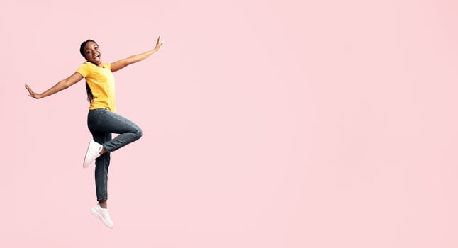 Carefree Lady. Happy African Woman Jumping In Air Posing Over Pink Studio Background. Full Length, Empty Space photo
