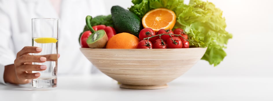 Professional nutritionist afro lady promoting healthy eating, offering water with lemon, fruits and vegetables photo