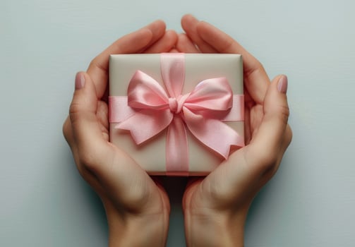 Close Up Of Two Hands Holding A Pink Gift Box With A Bow photo