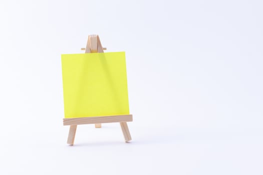 Wooden Easel Miniature with Blank Colored Square Canvas or Memo Paper - Mockup. Mini Wooden Stand with Clean Artboard on White Background, Copy Space photo