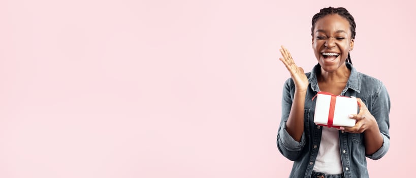 Birthday Concept. Happy Black Lady Holding Gift Box And Laughing Standing Over Pink Studio Background. photo