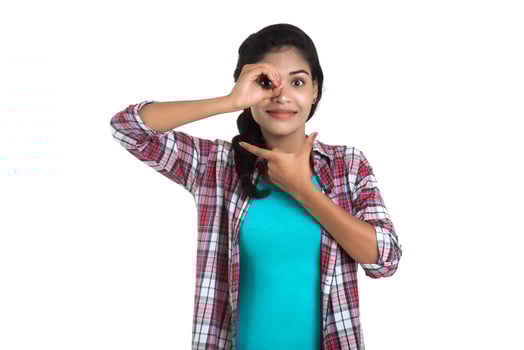 young woman looking at camera through fingers in ok gesture. Imitating binoculars over white background photo